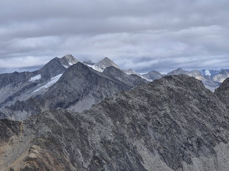 Reichenspitzgruppe im Detail mit der leider im Nebel verhüllten Reichenspitze sowie rechts dem Kuchelmooskopf, links ebenfalls im Nebel die Wildgerlosspitze, vorgelagert von links: Schneekarspitze, Zillerkopf und Schönachschneid, weiter hinten Zillerspitze, Richterspitze und Schwarzköpf; im Vordergrund Rötenspitze links und Höhenbergkarkopf